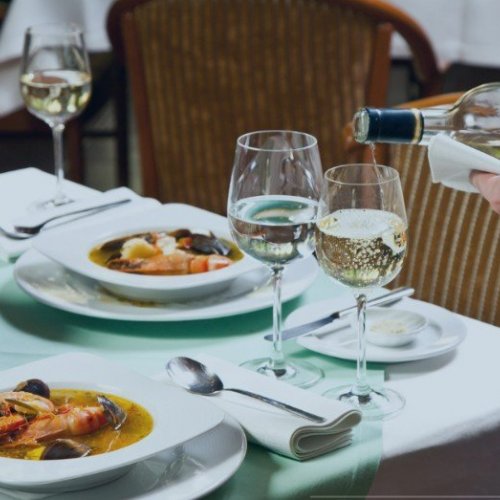 Foto de una mesa de un restaurante de mantel con copas de vino sirviéndose.